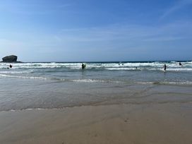 A beach with people in the water and a large rock formation in the distance at Penpraze in Portreath