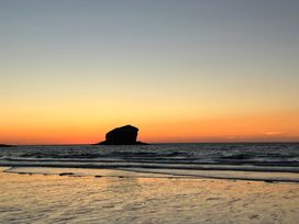 A beach scene at sunset with a large rock formation in the ocean and gentle waves at Penpraze in Portreath