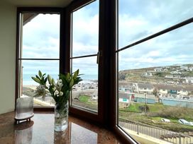 A window view showing a coastline with buildings and cars with flowers in a vase on the windowsill at Curnows Portreath