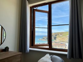A room with a wooden dresser a round mirror curtains an open window showing a coastal view with cliffs and the ocean at Curnows in Portreath