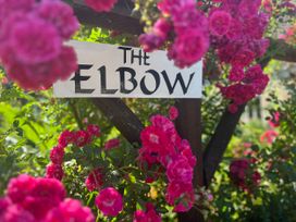 A sign labeled The Elbow surrounded by pink flowers at The Elbow in Frampton