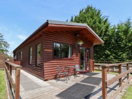 A wooden cabin with a deck and chairs at The Fallows Llanerch Park near St Asaph