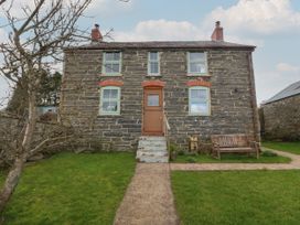 A stone house with a wooden door fronted by a pathway and green lawn with a bench on the right at Priddbwll in Llansannan