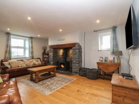 A living room with leather sofas a wooden coffee table a stone fireplace and a wall-mounted television at Priddbwll in Llansannan