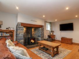 A living room with a stone fireplace wood stove leather sofa wooden coffee table and a wall mounted television at Priddbwll in Llansannan