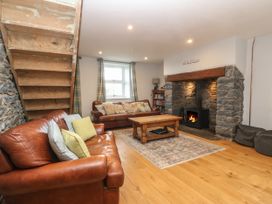 A living room with leather sofas a wooden coffee table a fireplace with stone surround and wooden stairs at Priddbwll in Llansannan