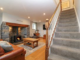 A living room with a staircase a stone fireplace a wood burning stove a leather sofa a wooden coffee table and a television at Priddbwll in Llansannan