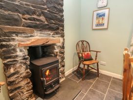 A corner with a wood burning stove set in a stone fireplace and a wooden chair with a cushion at Priddbwll in Llansannan