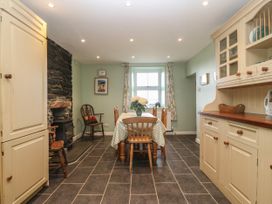 A kitchen dining room with a wooden table and chairs a stone fireplace and cream cabinets at Priddbwll in Llansannan