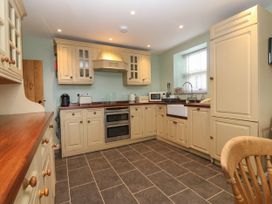 A kitchen with cream cabinets a wooden countertop a double oven a sink under a window and a wooden chair at Priddbwll in Llansannan