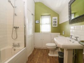 A bathroom with a bathtub and shower unit a toilet a sink and a window at Priddbwll in Llansannan