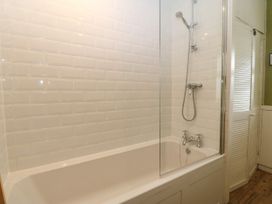 A bathroom with a white bathtub shower combination and white tiled walls at Priddbwll in Llansannan