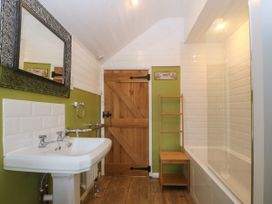 A bathroom with a sink mirror wooden door bathtub and wooden rack at Priddbwll in Llansannan