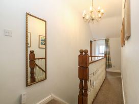 A hallway with wooden banister railing a wall mirror and a chandelier at Priddbwll in Llansannan