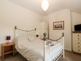 A bedroom with a white metal bed frame bedside tables with lamps a chest of drawers with a television and a framed picture on the wall at Priddbwll in Llansannan