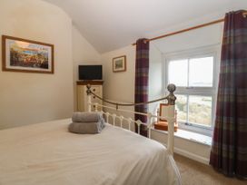 A bedroom with a bed with folded towels on it a small dresser with a television and a window with plaid curtains at Priddbwll in Llansannan