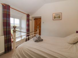 A bedroom with a bed and rolled towels near a window with plaid curtains at Priddbwll in Llansannan