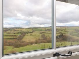 A view of green fields and hills through a window with a black handle at Priddbwll in Llansannan