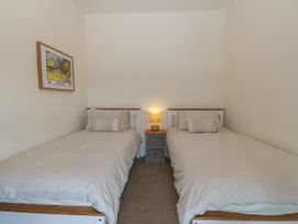 A bedroom with two single beds a nightstand with a lamp and a framed picture on the wall at Priddbwll in Llansannan