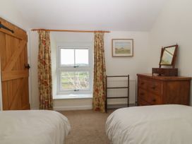 A bedroom with two beds a wooden dresser with a mirror a window with floral curtains and a wooden door at Priddbwll in Llansannan