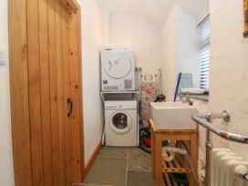 A utility room with a stacked washer and dryer a wooden sink unit and cleaning tools at Priddbwll in Llansannan