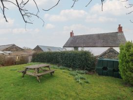 A garden with a wooden picnic table a hedge a green water tank and buildings in the background at Priddbwll in Llansannan