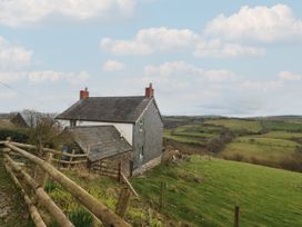 A countryside house with a wooden fence and green fields in the background at Priddbwll in Llansannan
