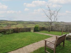 A garden with a wooden bench a pathway a stone wall and a view of green fields at Priddbwll in Llansannan