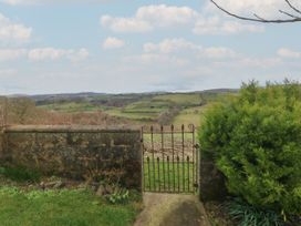 An iron gate in a stone wall opening to a view of green fields and rolling hills at Priddbwll in Llansannan
