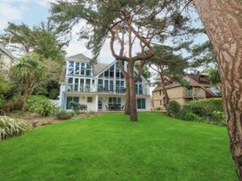 A house with large windows and balconies surrounded by trees and green lawn at 5 Red Sails in Sandbanks
