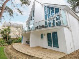 Exterior of a two story white house with a glass balcony and a patio area with chairs at 5 Red Sails in Sandbanks