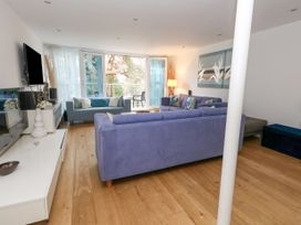 A living room with blue sofas a television on the wall and a glass door to a balcony at 5 Red Sails in Sandbanks