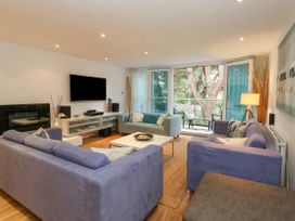 A living room with two blue sofas one grey sofa a white coffee table a wall mounted TV and glass doors opening to a balcony at 5 Red Sails in Sandbanks