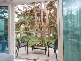 A balcony with two chairs and a table with fruit and wine overlooking trees and a garden at 5 Red Sails in Sandbanks