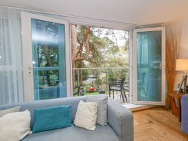A living room with a sofa facing open glass doors leading to a balcony with chairs and a table at 5 Red Sails in Sandbanks
