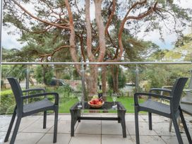 A balcony with two chairs a small table with a fruit bowl and wine glass overlooking trees and a garden at 5 Red Sails in Sandbanks