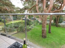 A balcony with glass railing overlooking trees and a lawn at 5 Red Sails in Sandbanks