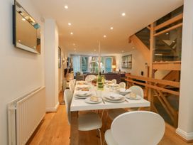 A dining room with a table set for eight people and a living area with sofas and large windows at 5 Red Sails in Sandbanks