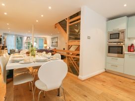 A dining area with a set table of plates and glasses next to a kitchen with built in oven and microwave and wooden staircase in the background at 5 Red Sails in Sandbanks