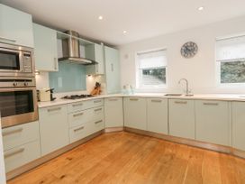 A kitchen with light green cabinets a gas stove a built in oven microwave double windows a sink and wooden floor at 5 Red Sails in Sandbanks