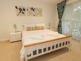 A bedroom with a white bed with pillows and folded towels and nightstands with lamps and patterned curtains at 5 Red Sails in Sandbanks