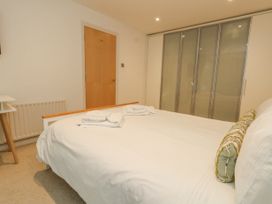 A bedroom with a bed with white bedding and pillows folded towels on top a wooden door a radiator a bedside table and wardrobes with sliding doors at 5 Red Sails Sandbanks