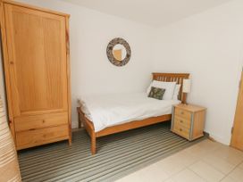 A bedroom with a wooden single bed a bedside table with a lamp a wooden wardrobe and a round wall mirror at 5 Red Sails in Sandbanks