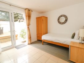 A bedroom with a single bed a wooden wardrobe a bedside table with a lamp and sliding glass doors with curtains leading outside at 5 Red Sails in Sandbanks