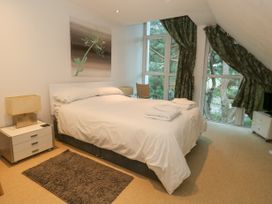A bedroom with a bed white bedding bedside tables lamps a dark rug and large windows with green curtains at 5 Red Sails in Sandbanks