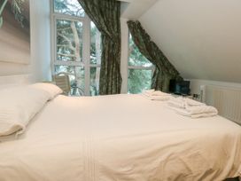 A bedroom with a bed covered with white linens two sets of folded white towels two windows with green curtains a small television and a chair at 5 Red Sails in Sandbanks