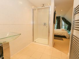 A bathroom with tiled floor glass shower enclosure glass sink and a view into a bedroom with a bed and windows at 5 Red Sails in Sandbanks