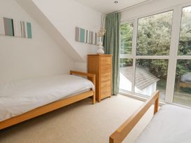 A bedroom with two single beds a chest of drawers and large windows showing trees outside at 5 Red Sails in Sandbanks