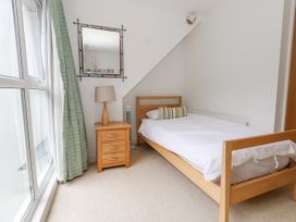A bedroom with a wooden single bed a bedside table with a lamp a wall mirror and green curtains at 5 Red Sails Sandbanks