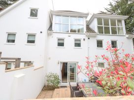 The back view of a white multi-story house with multiple windows and a sliding glass door opening to a patio with outdoor furniture and red-leaved plants at 5 Red Sails in Sandbanks